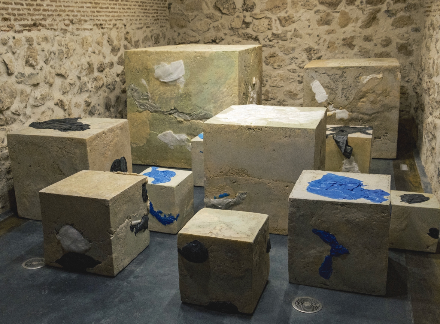 All Tangled Up in a Fading Star — a field of monumental concrete and polyurethane blocks embedded with reclaimed plastics, installed in a vaulted brick gallery.