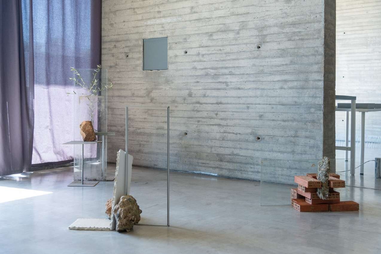 Installation view of SHIH: Thirteen Moons at C3A Córdoba — clay, copper, glass and brick assemblages with Artemisia standing against a raw concrete wall.